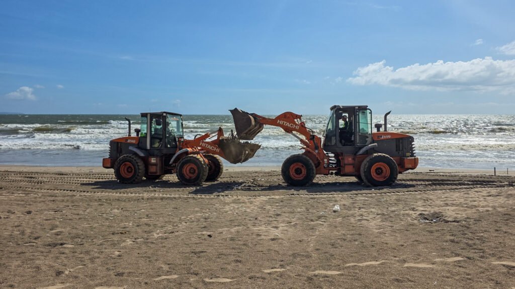 Machines and workers removing plastic debris from a Bali beach after ocean currents carried waste ashore.