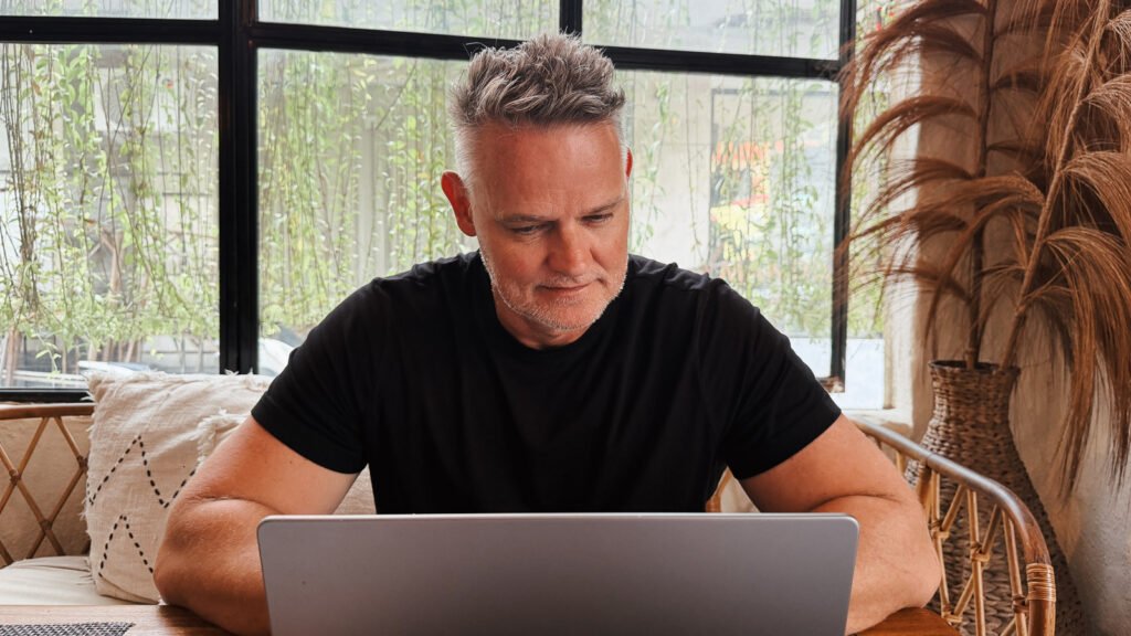 Person working on a laptop in a café, reflecting on content creation and online communities.