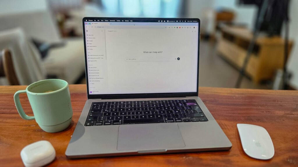 Laptop, mouse, coffee cup and earplug case on a minimalist desk in natural light