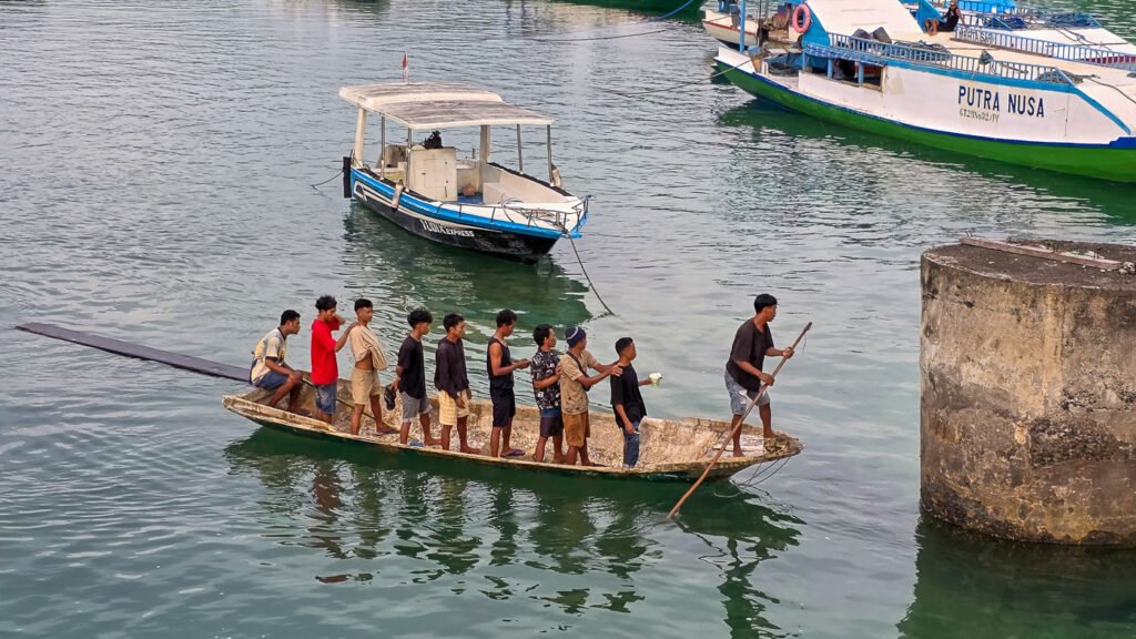 Small boat carrying ten men standing closely together while one man steers between Lembongan and Ceningan
