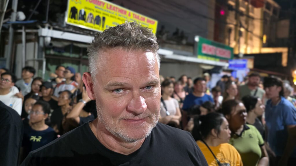 Man standing among a crowd of Balinese locals, visually distinct as the only Caucasian, representing standing out from a group.