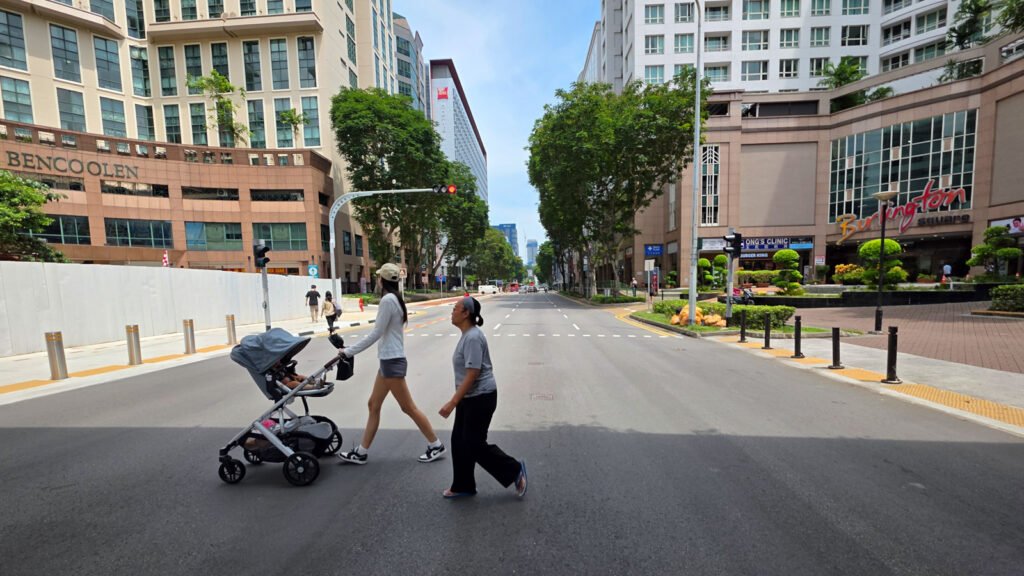 An older woman and a young mother with a baby carriage crossing a quiet street in Singapore.