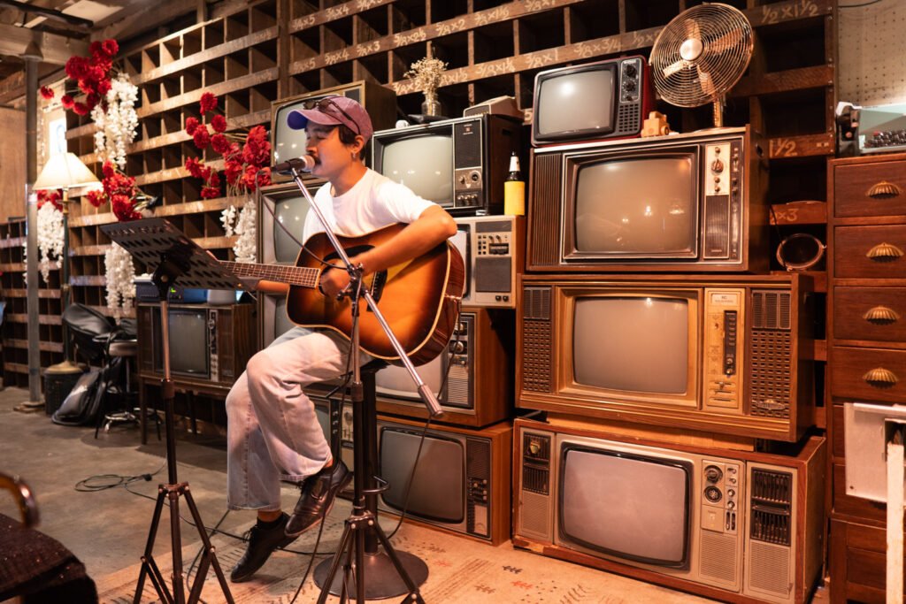 Acoustic guitarist performing in front of vintage CRT televisions in Thailand.