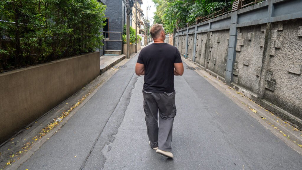 A man walking down a quiet side street in Bangkok, symbolizing observation, experience, and exploring the world firsthand.