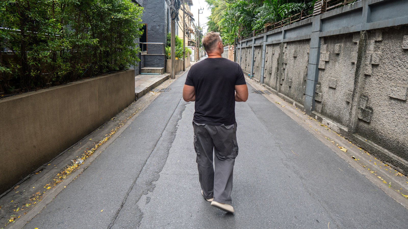 A man walking down a quiet side street in Bangkok, symbolizing observation, experience, and exploring the world firsthand.