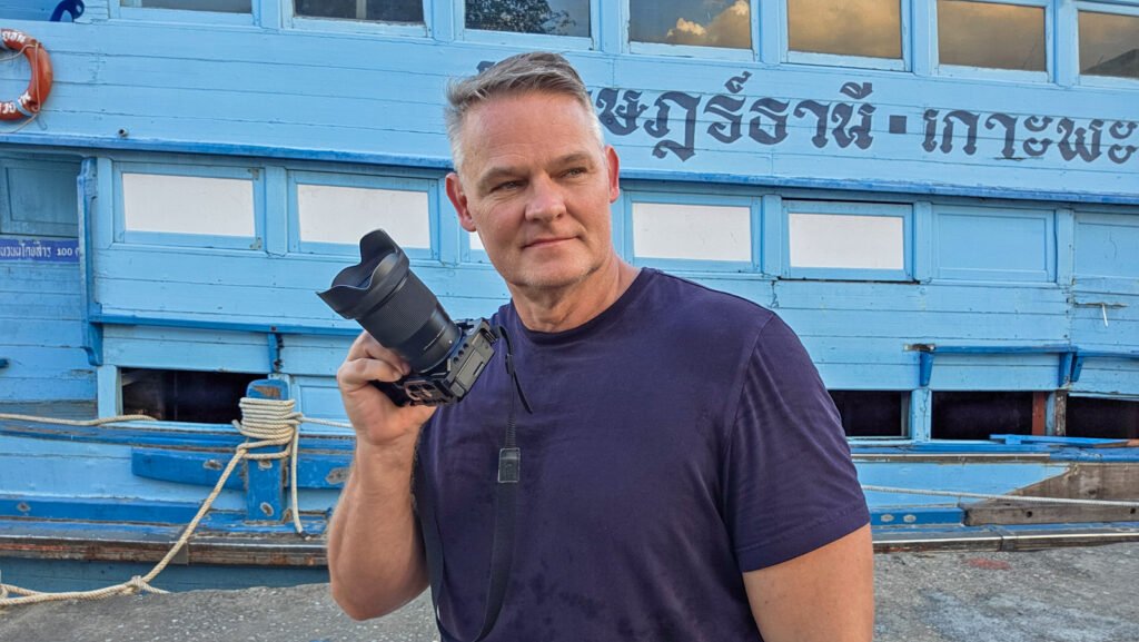 Martin holding a camera while looking toward the streets of Surat Thani, Thailand.