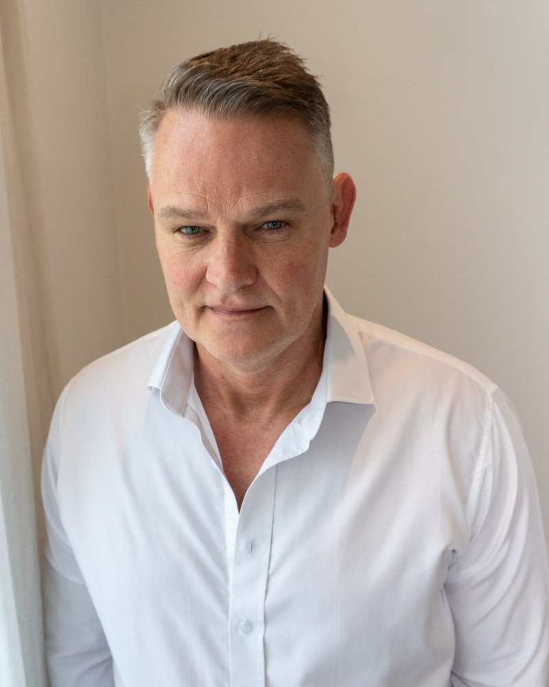 Martin Gram wearing a white shirt, standing beside a window.